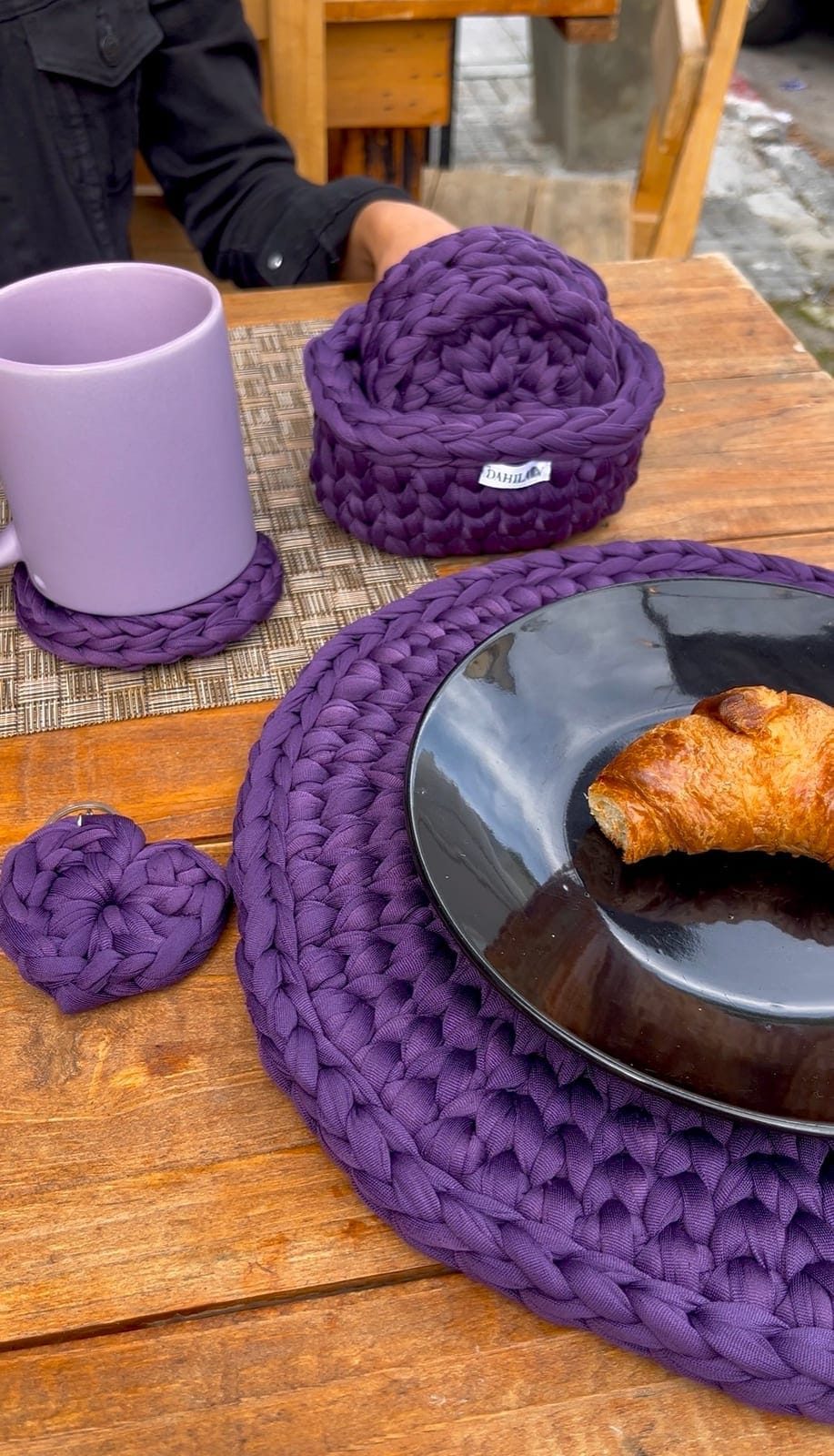 Piezas tejidas a crochet en trapillo violeta sobre una mesa: canasta, posavasos y un llavero con forma de corazón